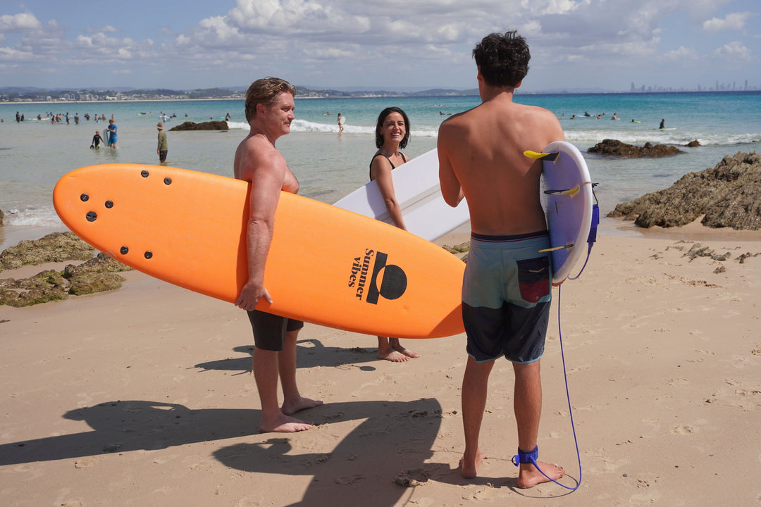 Surfers carrying a Summer vibes softboard and epoxy surfboards at Rainbow Bay