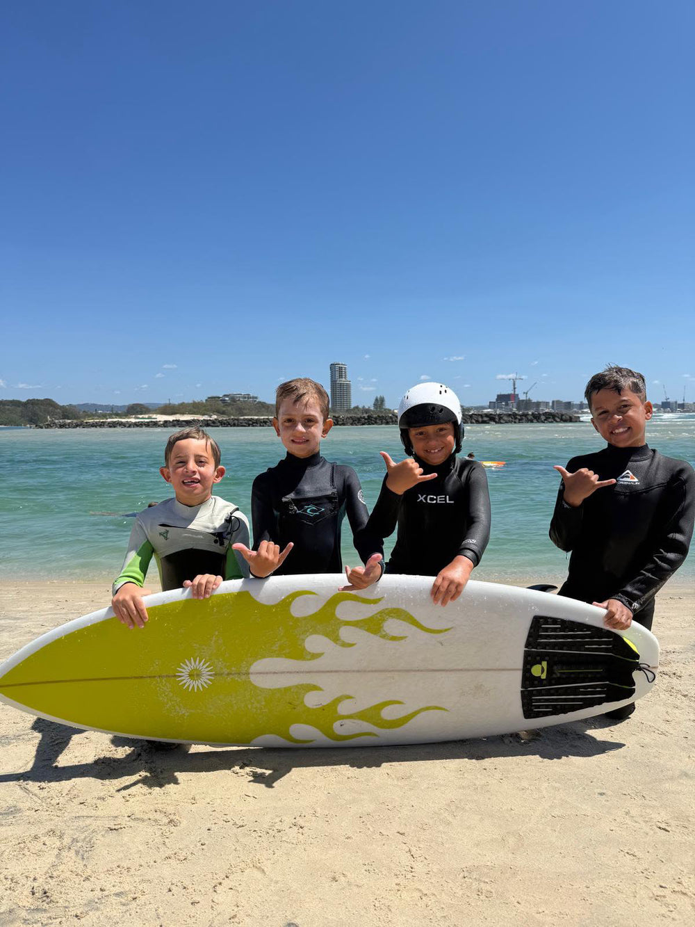 Four young surfers at the beach with a Summer vibes yellow flame Grom surfboard