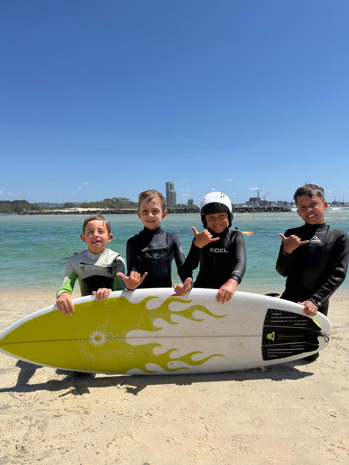 Four young surfers at the beach with a Summer vibes yellow flame Grom surfboard